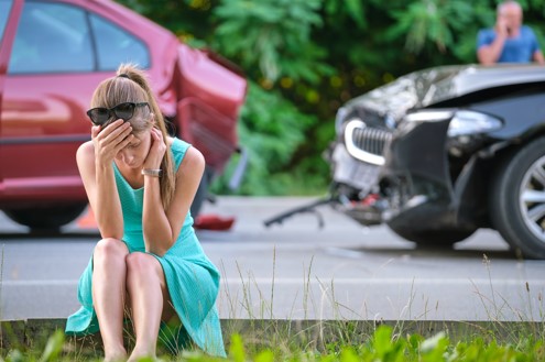 injured woman sitting on road beside car wreck