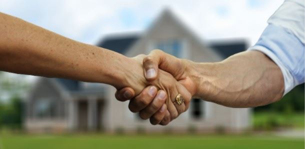 man and woman shaking hands with house in the background